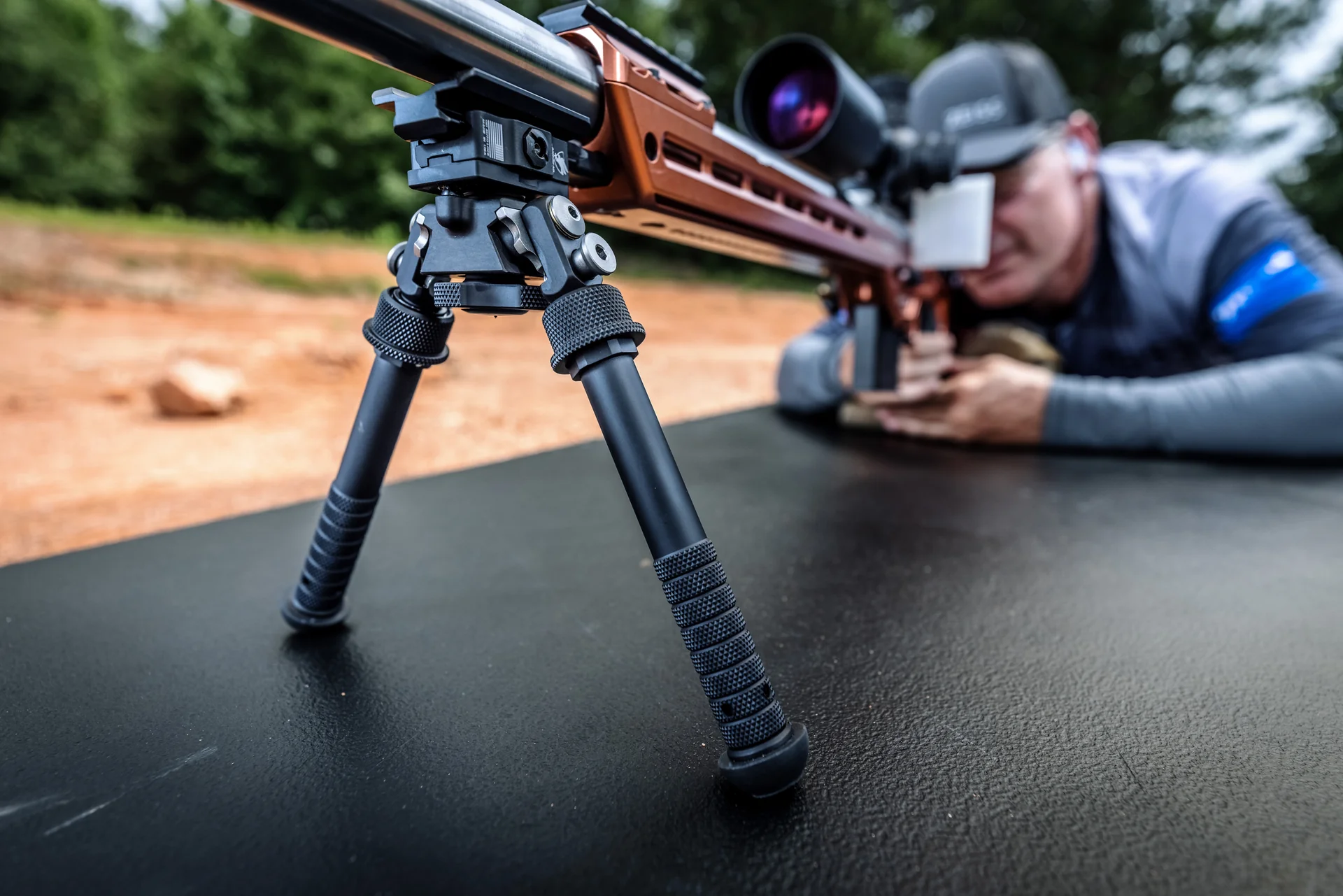 Atlas bipod deployed under an orange-chassis precision rifle showing its pan and cant body as a shooter aims downrange.