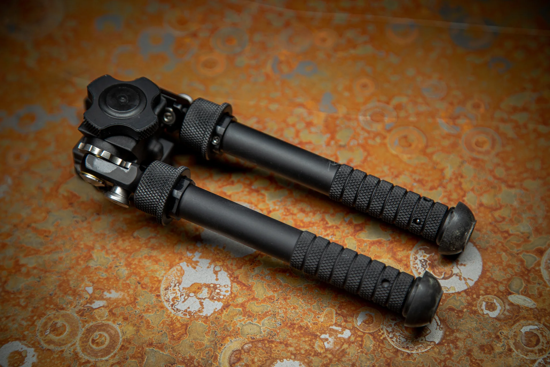 Atlas bipod shown folded with notched aluminum legs and pan-cant body in a studio detail on a rust background.