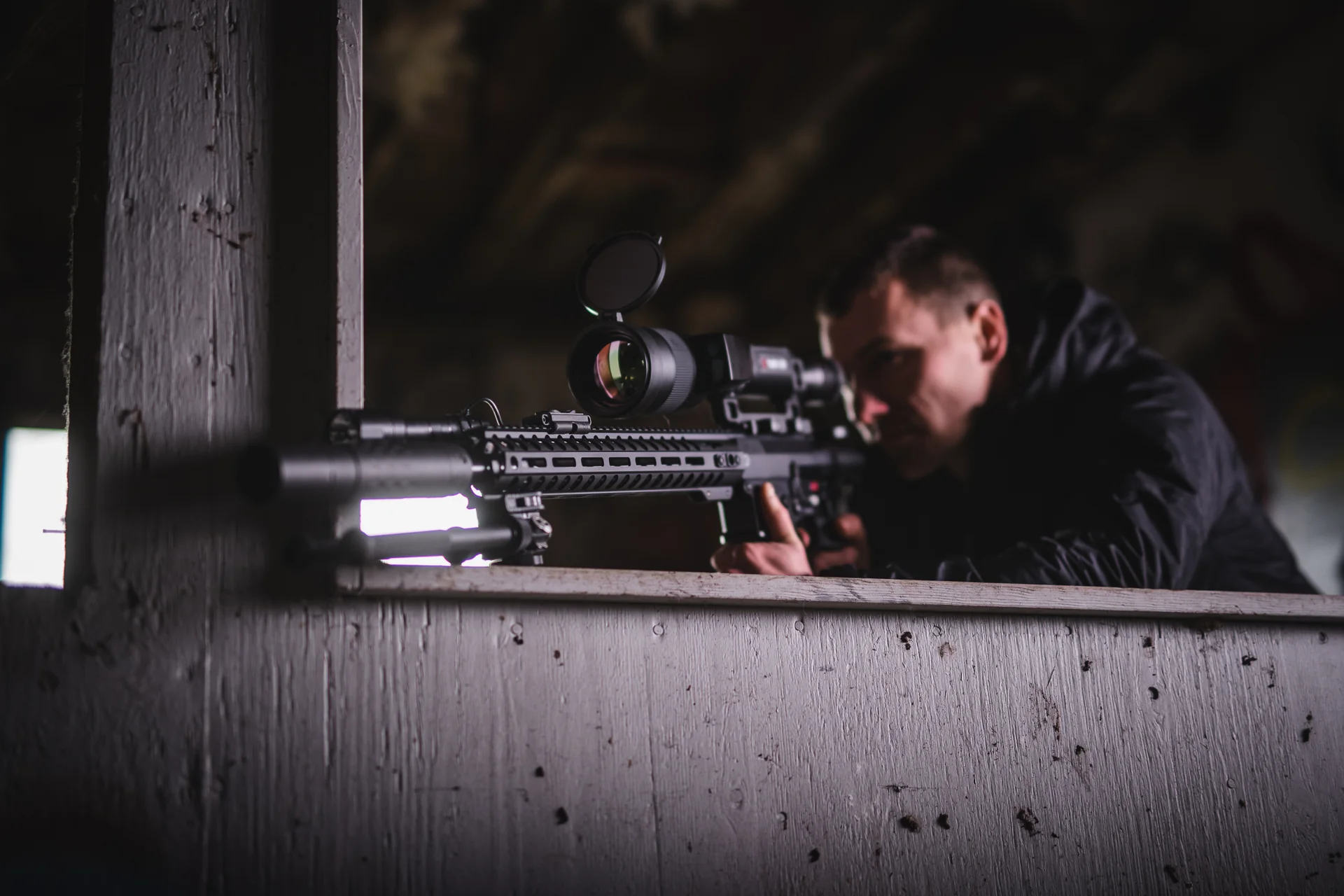 Folded Atlas bipod under an AR-10 thermal-scoped rifle resting on a wooden window ledge as a shooter aims outward.