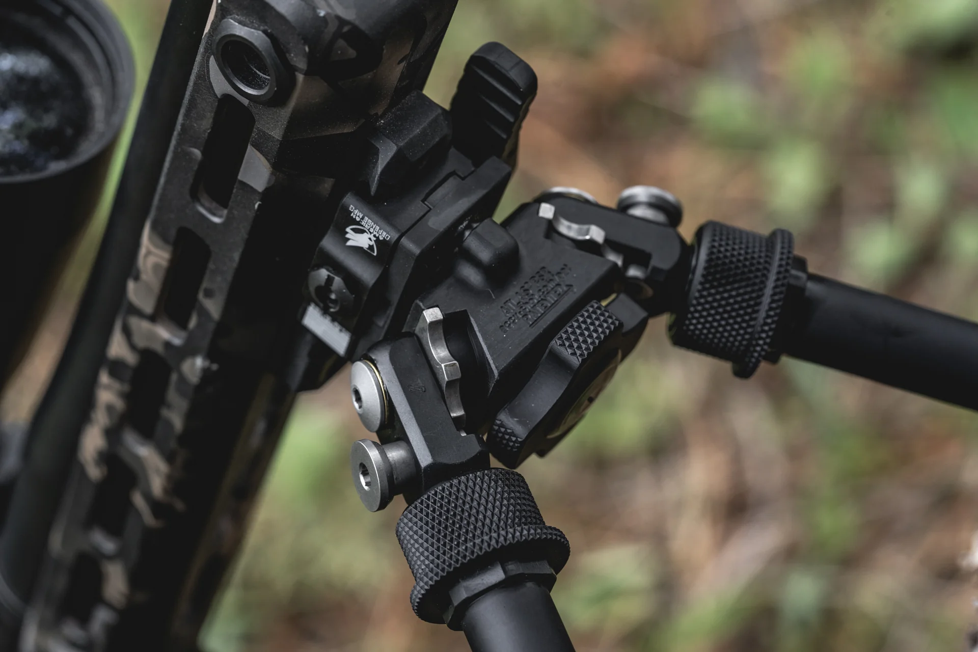Atlas bipod head detail deployed under a camo rifle showing the pan-and-cant body and notched legs.