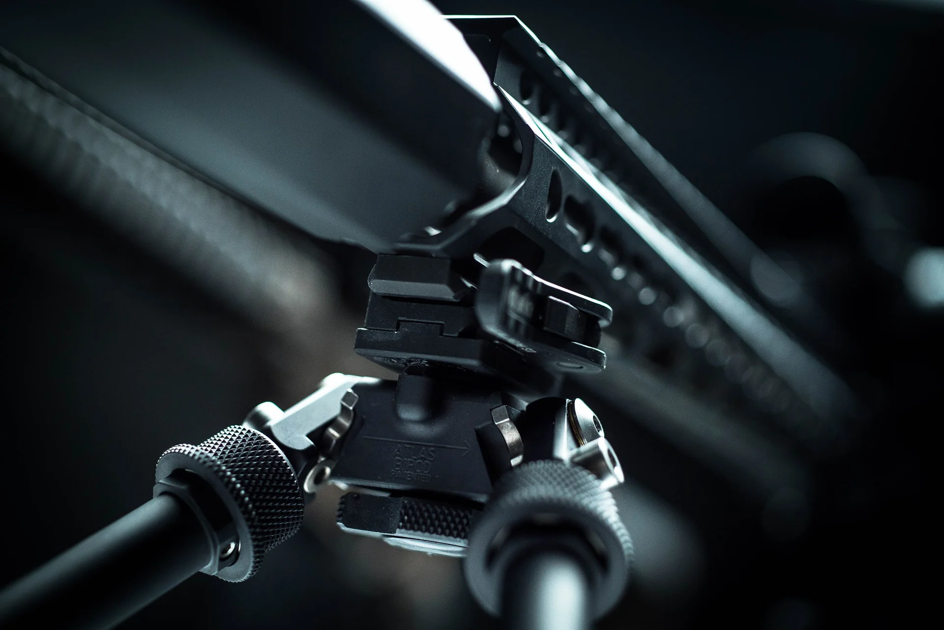 Atlas bipod close-up showing patented pan-and-cant body and rail mount beneath a precision rifle fore-end.