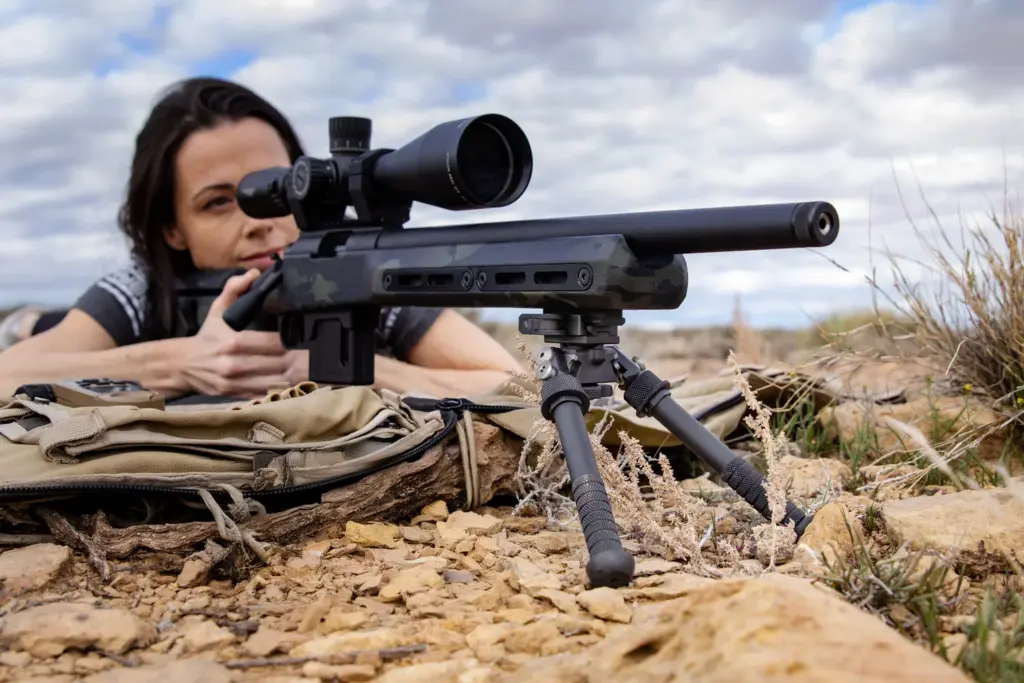 Shooter prone in the desert aiming a chassis rifle supported by the Atlas PSR BT46-LW17 bipod