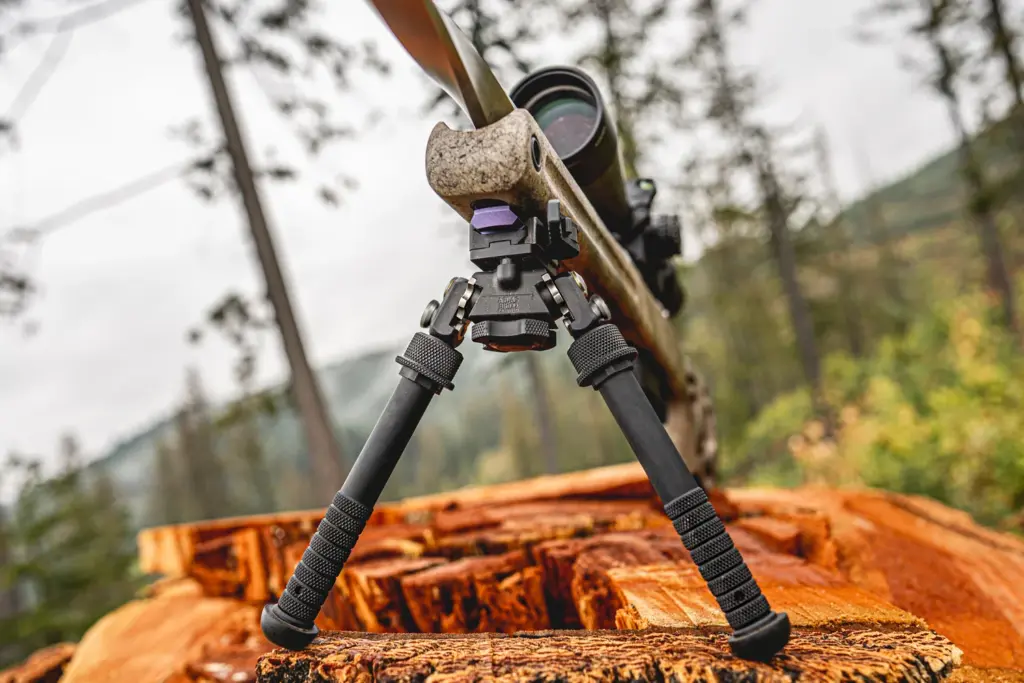 Rear view of a rifle resting on the Atlas PSR BT46-LW17 bipod atop a stump in the forest