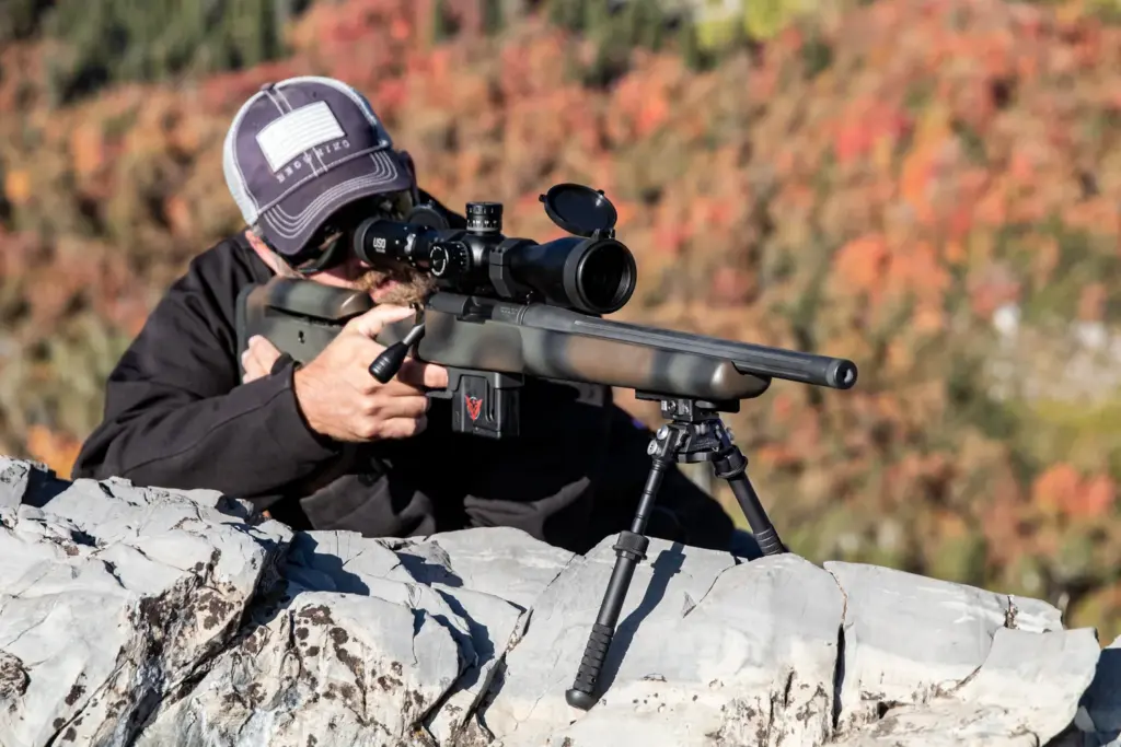Shooter aiming from a rock ledge over an autumn valley with the Atlas PSR BT46-LW17 bipod